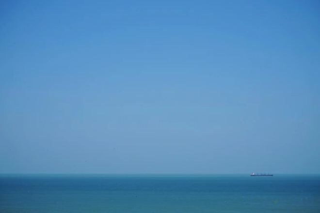 A clear sky over a calm sea with a distant ship.