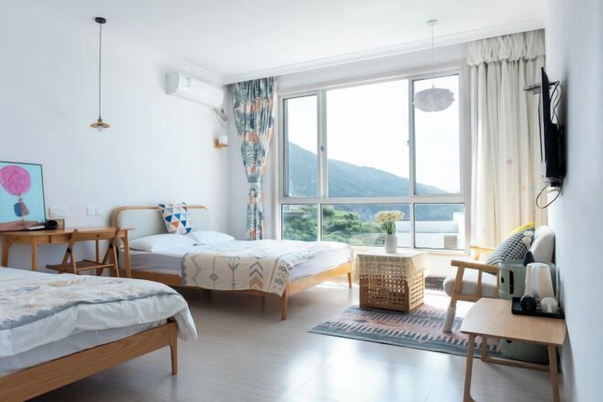 Une chambre avec deux lits, un bureau, une chaise, une télévision et une grande fenêtre donnant sur un beau paysage.