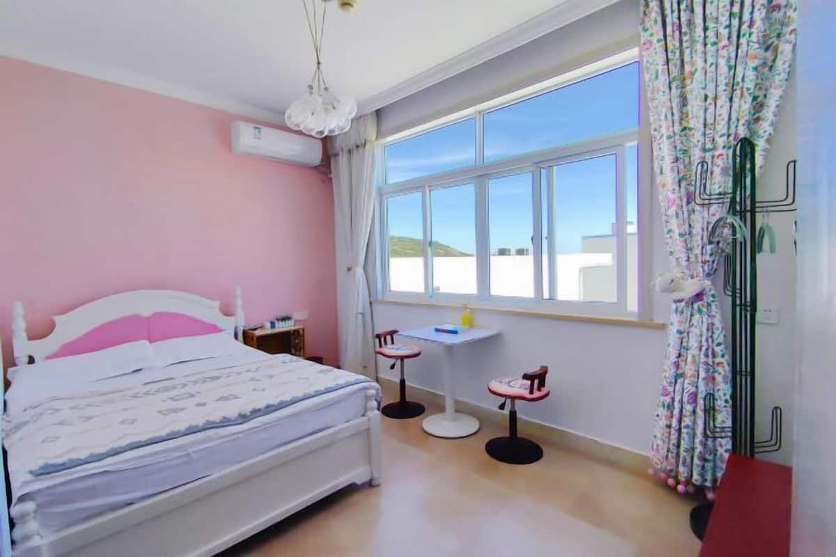 Een slaapkamer met een bed, een klein tafeltje, twee stoelen, een raam met uitzicht en een wandairconditioner.