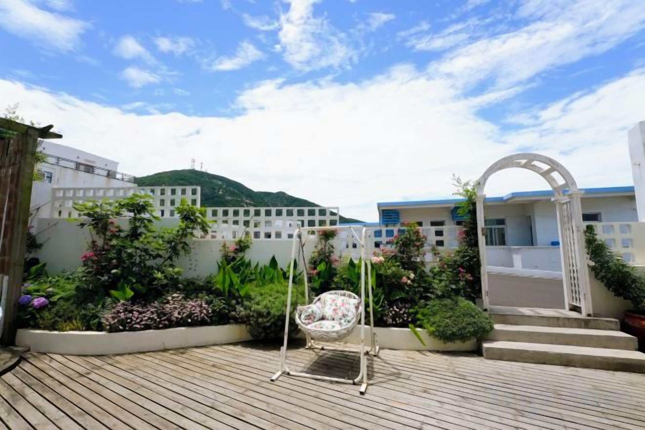 A wooden deck with a swing chair, a white archway, and a garden with various plants.