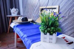 Une pièce avec un lit, une petite table sur laquelle se trouve une théière, et une plante en pot ornée de fleurs.