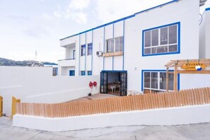 Un bâtiment moderne à la façade blanche et aux touches de bleu, doté d’un balcon et d’une terrasse en bois.