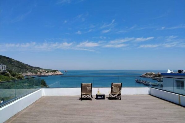 A balcony with two chairs and a small table, overlooking a coastal area with clear skies. - Huaniao Island Banshan Banhai Hostel (Shengsi)
