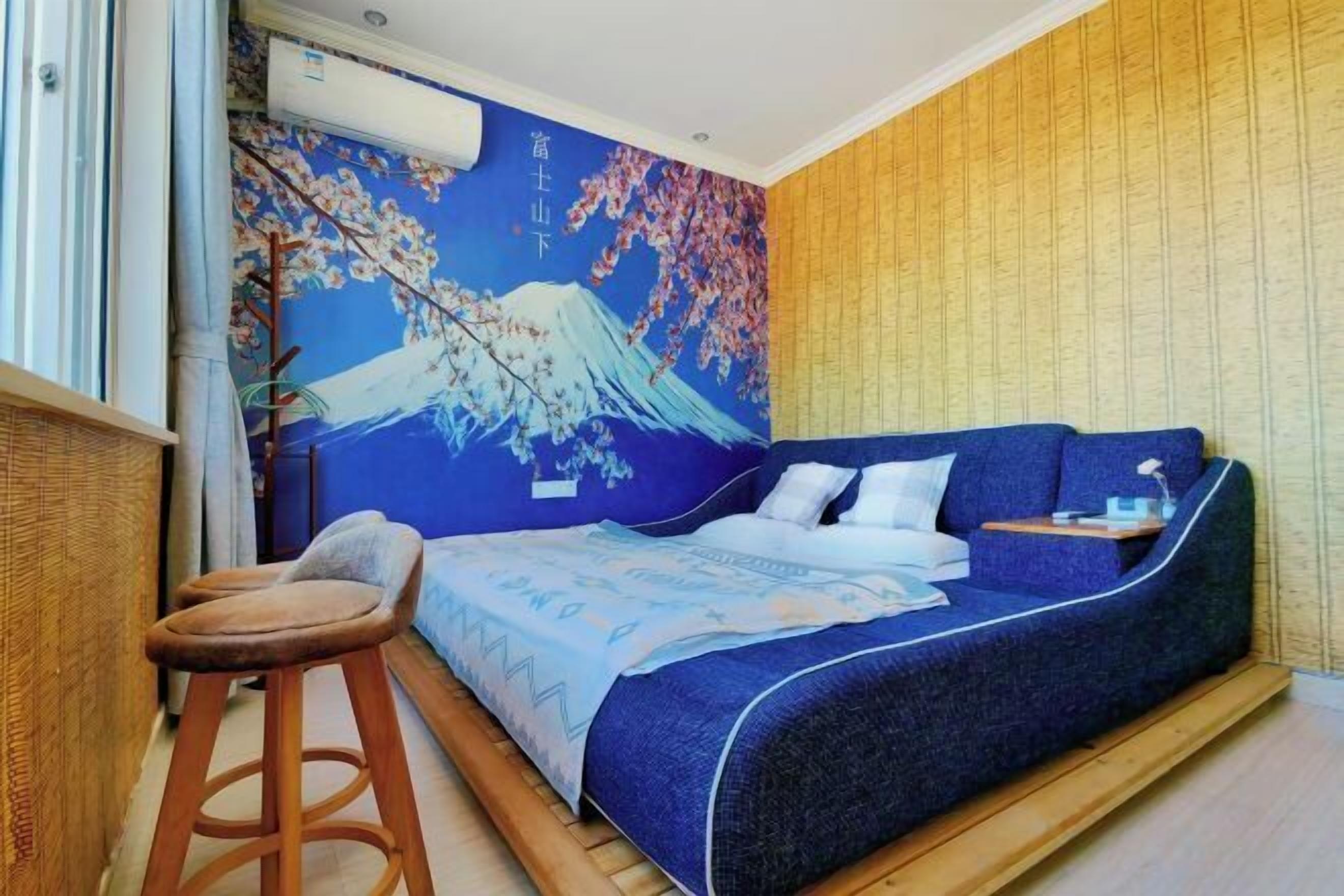 A room with a bed, a stool, a wall with a painting, and a window.