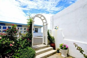 A white building with a wooden staircase leading to an arched entrance, surrounded by potted plants and flowers. - Huaniao Island Banshan Banhai Hostel (Shengsi)