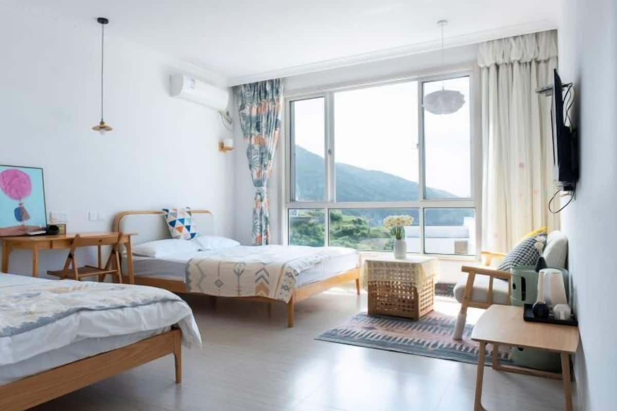 Een slaapkamer met twee bedden, een bureau, een stoel, een televisie en een groot raam met uitzicht.