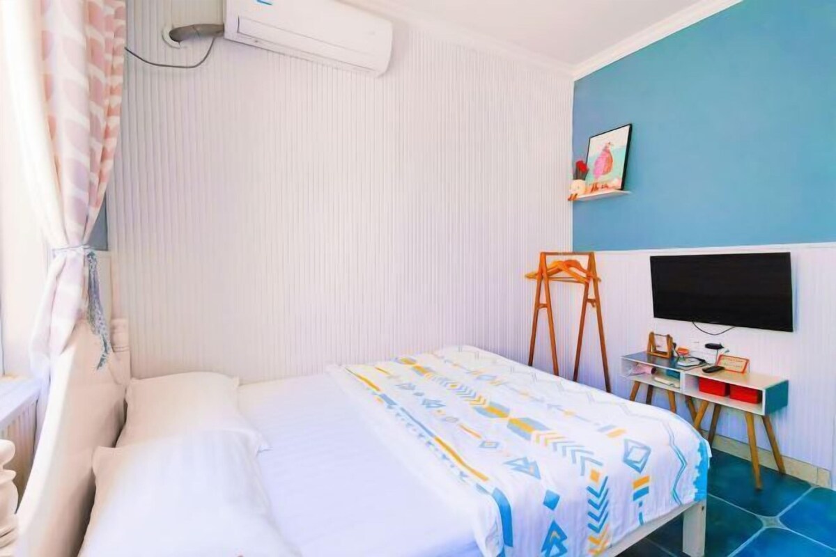 Une chambre à coucher comprenant un lit, un bureau, une chaise, un téléviseur et un climatiseur fixé au mur.
