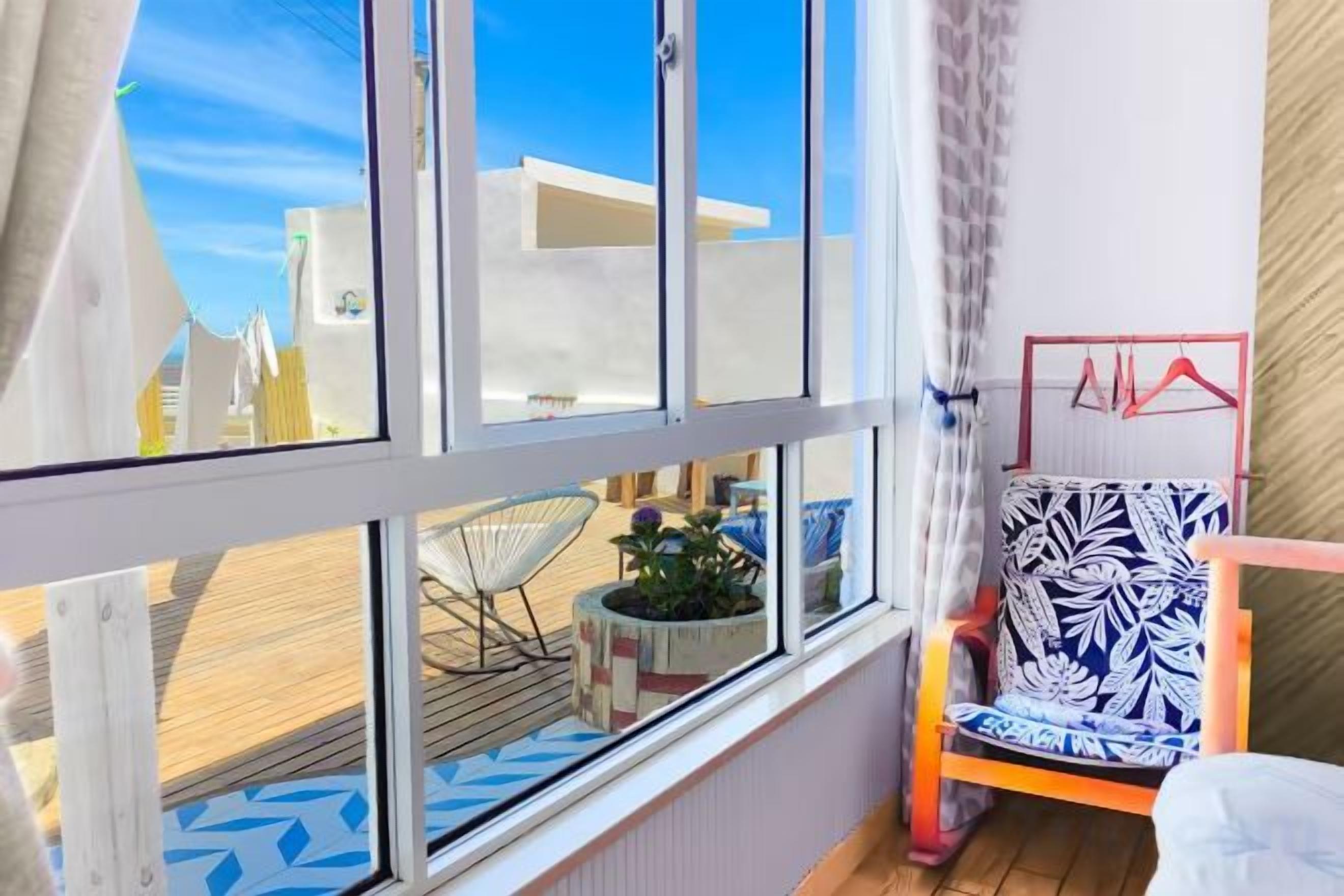 Ein Zimmer mit einem großen Fenster, einem Sessel mit gemustertem Kissen und einem kleinen Tisch mit Pflanze.
