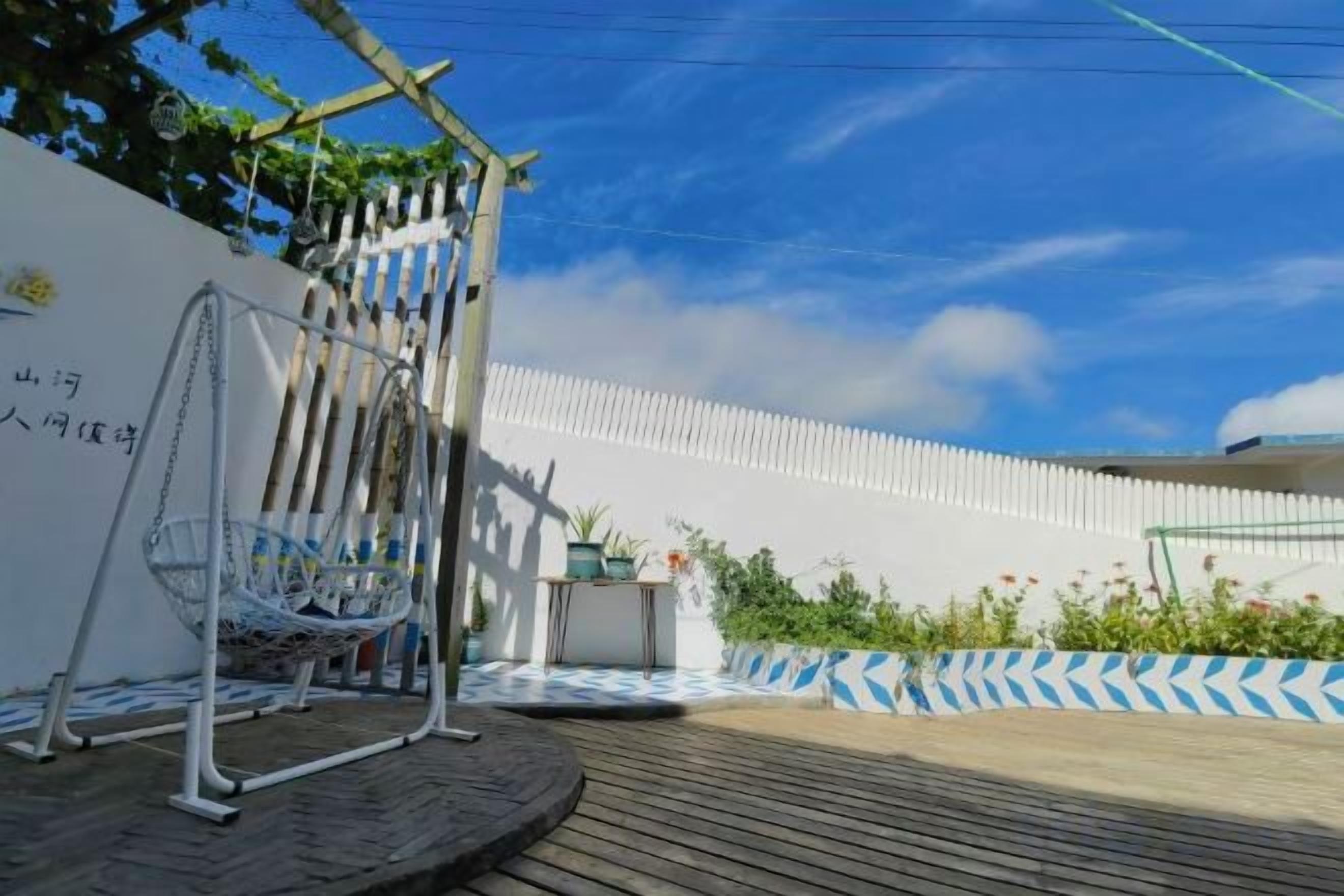 A wooden deck with a hanging chair, a white wall with text, and a blue and white chevron-patterned wall.