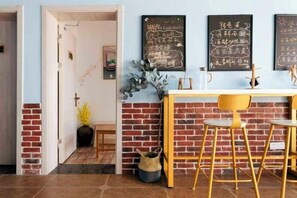 A room with a brick wall, a wooden table, and a yellow chair. There are chalkboards with writing on the wall. - Huaniao Island Banshan Banhai Hostel (Shengsi)