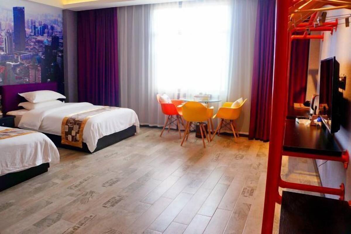 A hotel room with two beds, a dining table with four chairs, a TV, and a cityscape mural on the wall.