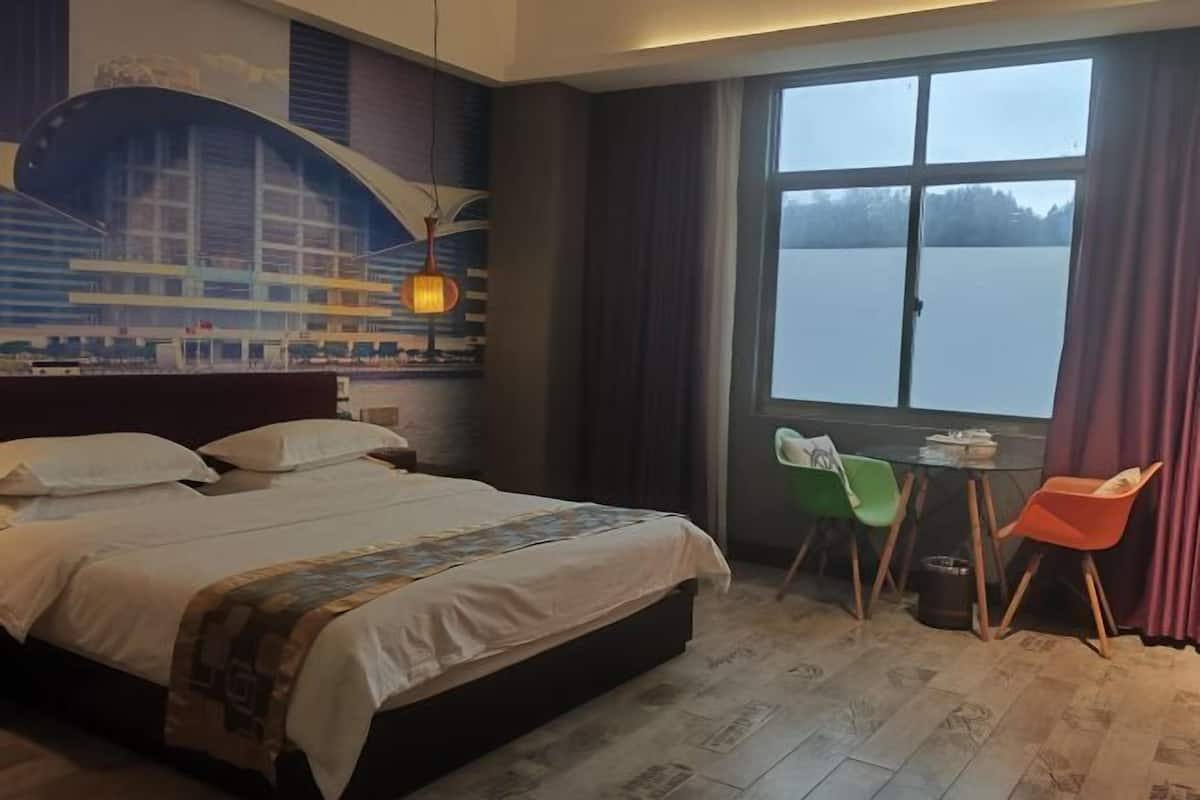 A hotel room with a bed, a small table, two chairs, a window with a view, and a mural on the wall.
