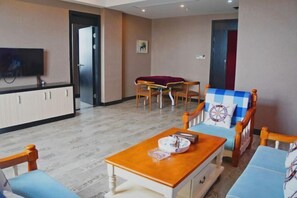 Ein Hotelzimmer mit einem Holztisch, zwei Stühlen, einem Sofa, einem Fernseher und einer Tür zu einem weiteren Raum.