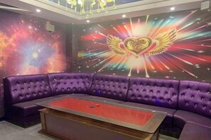 Ein violettes Sofa und ein roter Tisch in einem Raum mit Wandgemälde von Sternen und einem Herzen mit Flügeln.