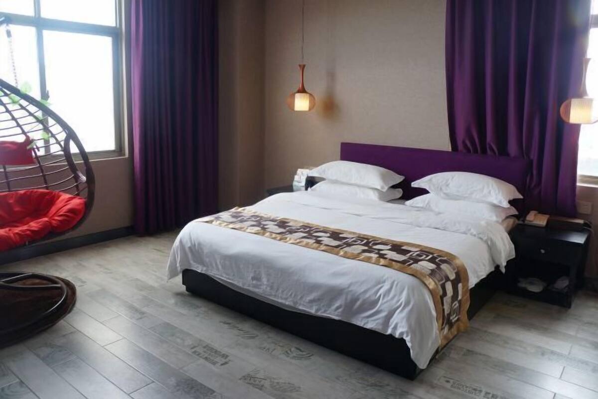 A bedroom with a bed, a hanging light fixture, a chair, and a window with curtains.