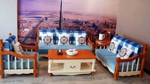 Ein Zimmer mit einer großen Stadtansicht als Wandgemälde, einer blau-weiß karierten Sofagarnitur, einem Holztisch und passenden Sesseln.