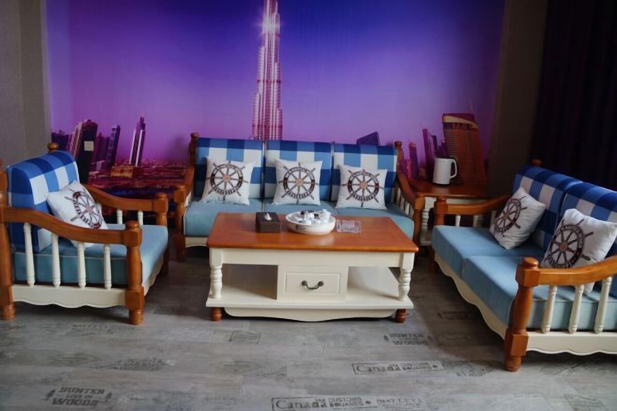 Ein Wohnzimmer mit einer gepolsterten Couchgarnitur in Karomuster, einem Couchtisch und Blick auf eine Stadtlandschaft im Hintergrund.