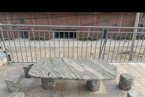 Un banco de piedra con cuatro patas, ubicado en un espacio al aire libre con una valla metálica de fondo.