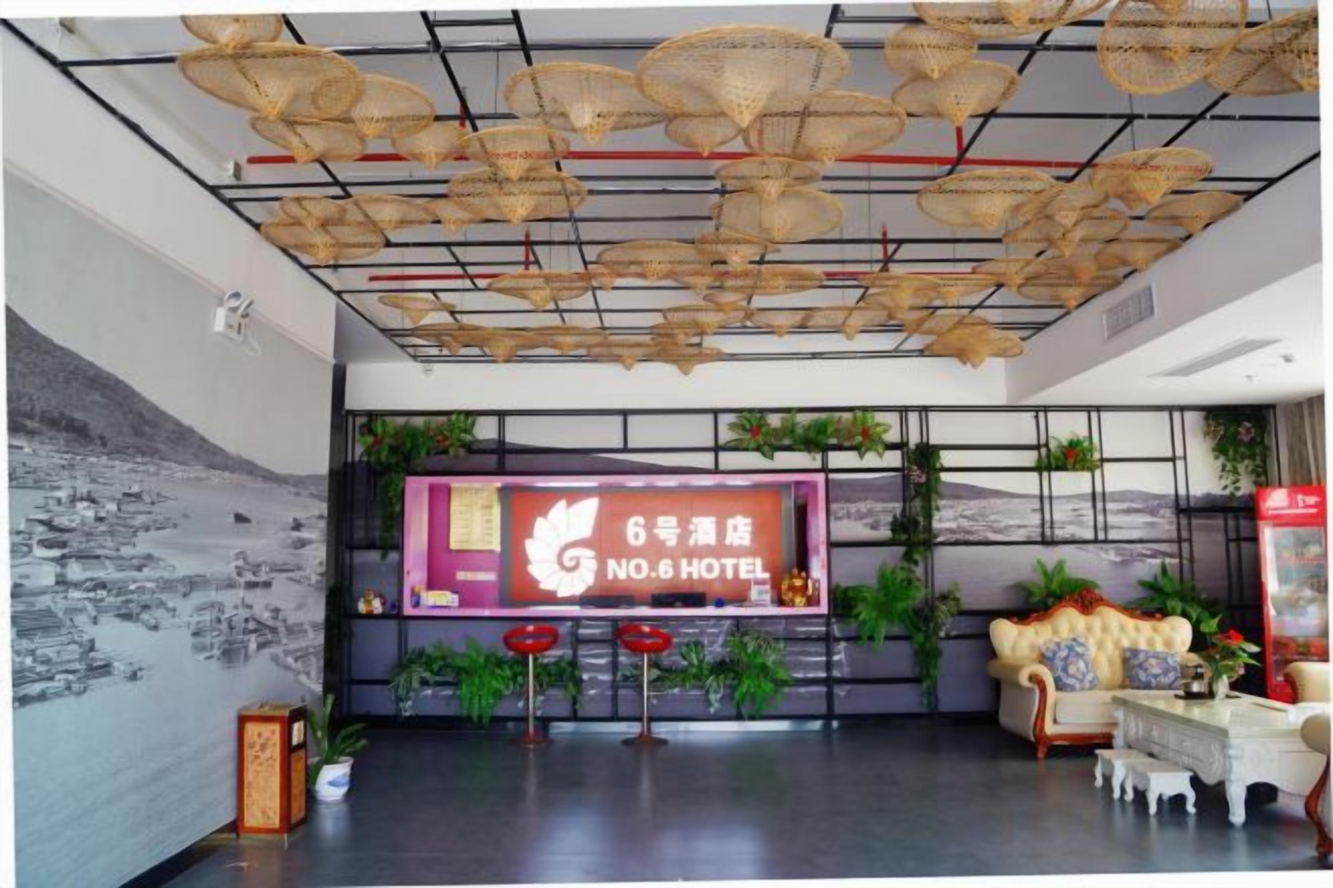 A hotel lobby with a large reception desk, a wall-mounted sign, and several potted plants.