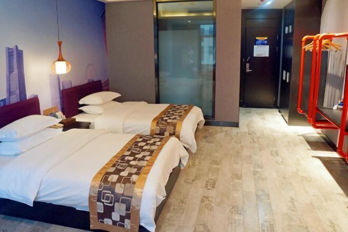 Ein Hotelzimmer mit zwei Betten, einer Stadtlandschaft als Wandbild, einer Glasabtrennung und einem roten Ablagegestell.