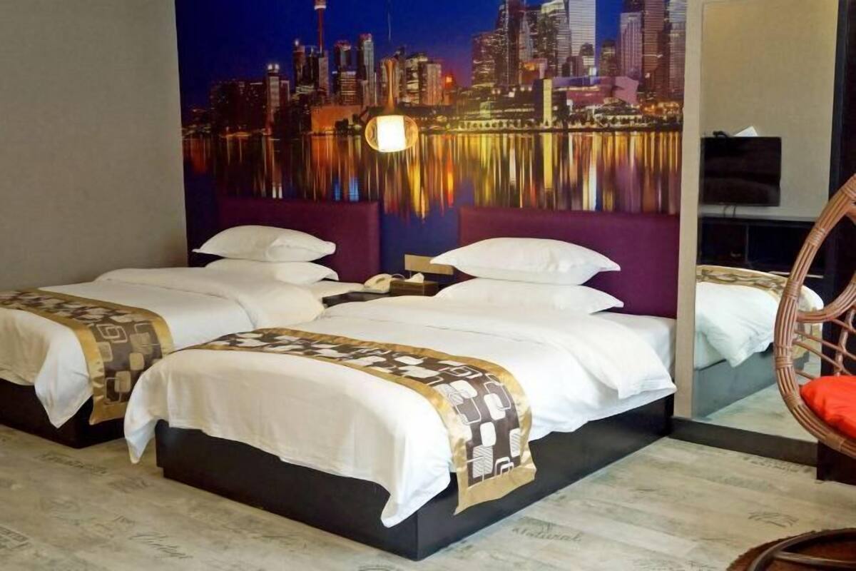 A hotel room with two beds, a cityscape mural, a television, and a wicker chair.