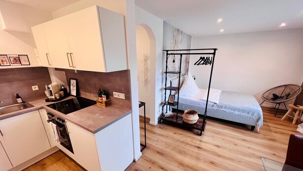 A compact kitchen with modern appliances, a dining area, and a bed with a hanging clothes rack. - Casa Wedel (Lampertheim)