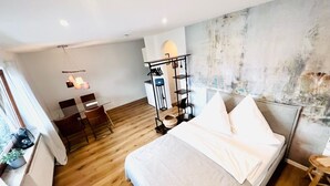 A modern bedroom with a wooden floor, a bed with white linens, a desk with a chair, and a clothing rack. - Casa Wedel (Lampertheim)