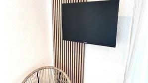 A modern room with a mounted TV, a wicker chair, and a small wooden stool. - Casa Wedel (Lampertheim)