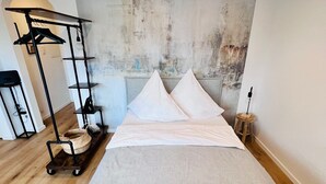 A bedroom with a large bed, a wooden floor, a wall-mounted shelf with a basket, and a hanging light fixture. - Casa Wedel (Lampertheim)