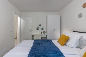 A bedroom with a bed, white wardrobe, and a desk with a chair.