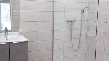 A modern bathroom with a glass-enclosed shower, a sink with a mirror, and a trash bin.