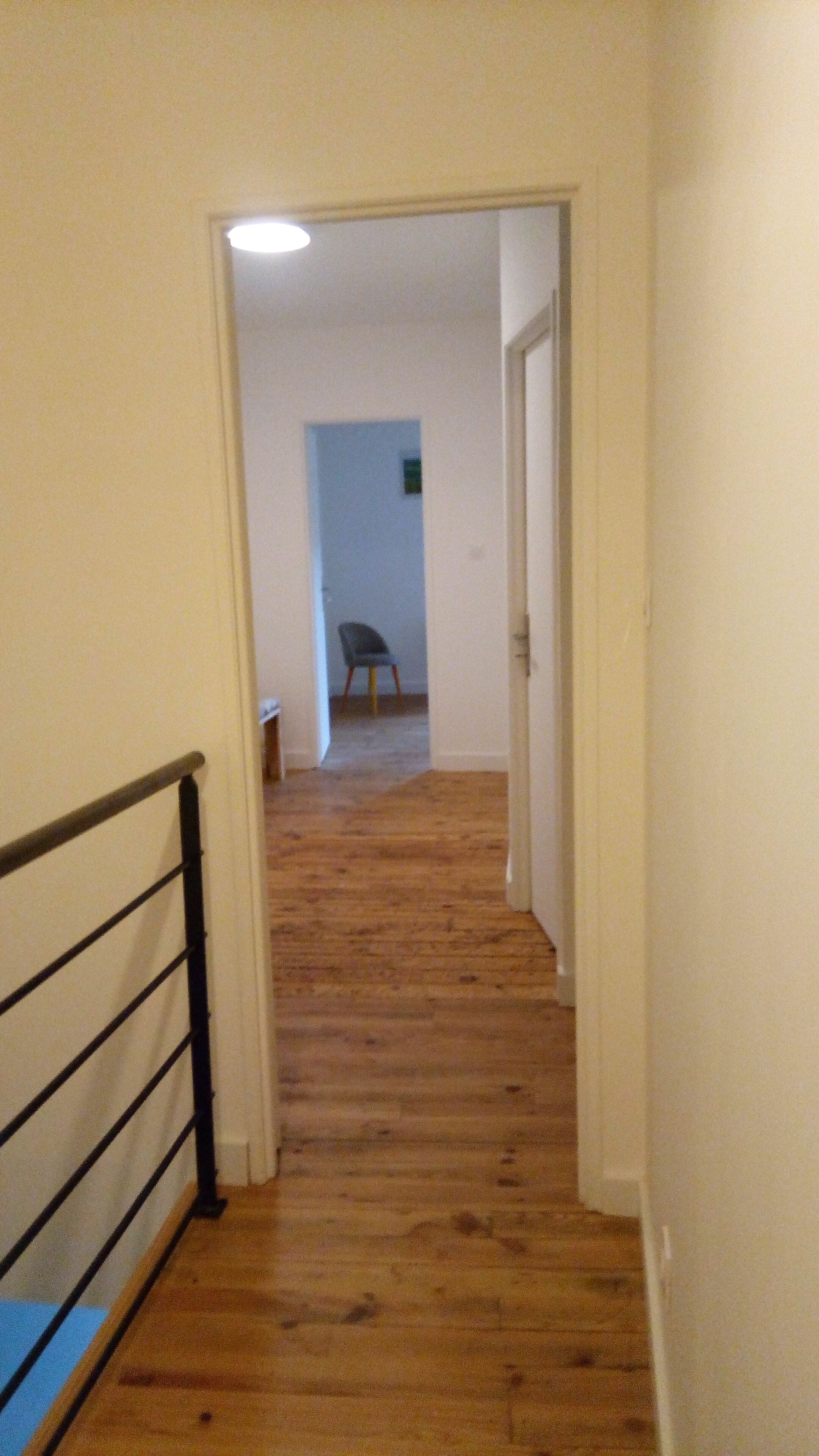 Un couloir au plancher de bois mène à une pièce où se trouvent une chaise et une petite table.
