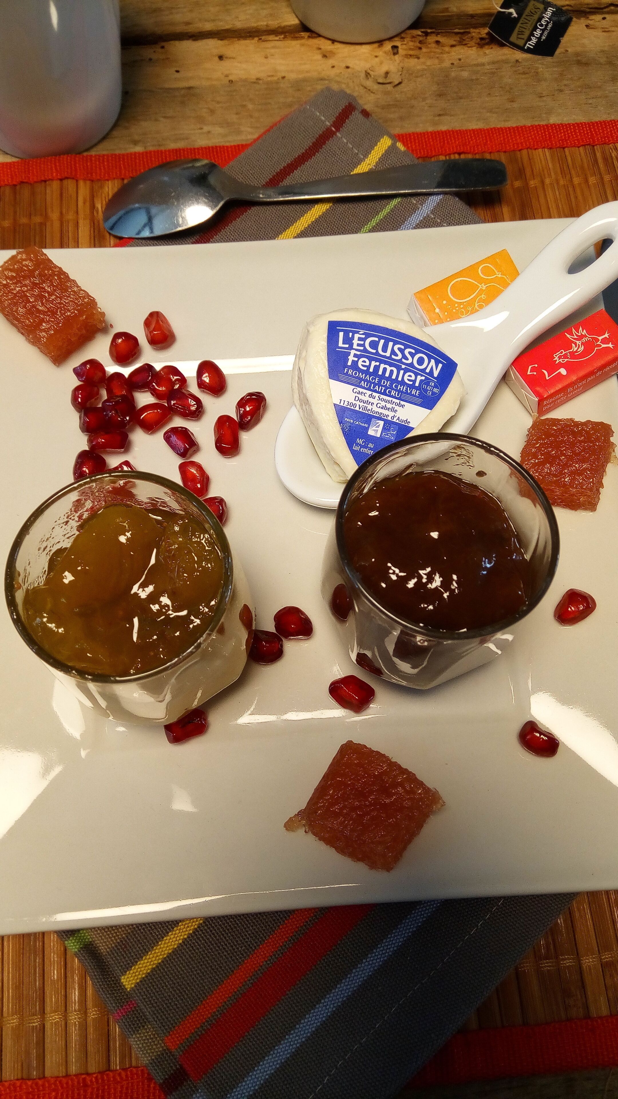 Un plat blanc amb dues copes de confitura, un tros de formatge i llavors de melgranada disperses.