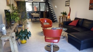 A modern living room with a black leather sofa, a red chair, and a staircase.