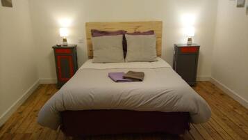 A neatly made bed with a wooden headboard, two bedside tables with lamps, and a wooden floor.