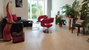 A modern living room with a black sofa, red chairs, a glass coffee table, and a large window with a view of greenery.