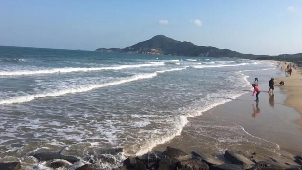 A beach with waves, people, and a mountain in the background. - Yumei Inn (Dongshan County)