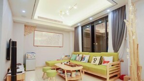 A modern living room with a green sofa, wooden coffee table, and a TV on a stand. - Yumei Inn (Dongshan County)