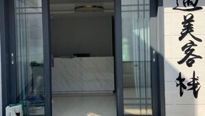 A hotel entrance with a sliding glass door, a reception desk, and a sign with Chinese characters. - Yumei Inn (Dongshan County)