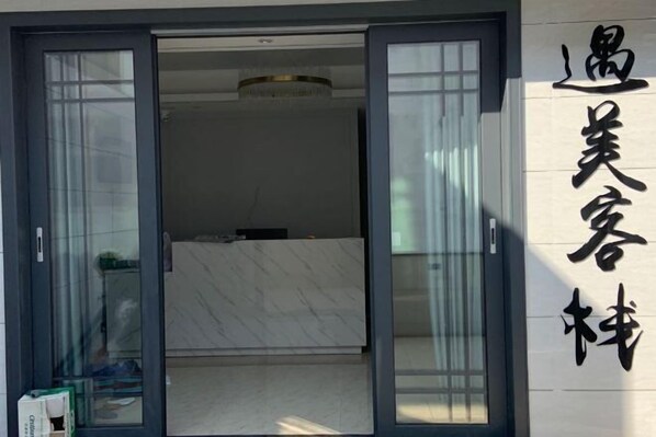 L’entrée d’un hôtel, avec une porte coulissante en verre, un comptoir d’accueil et une enseigne avec des caractères chinois.