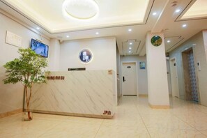 Un comptoir d’accueil avec un plateau en marbre, une petite plante en pot et une horloge au mur.