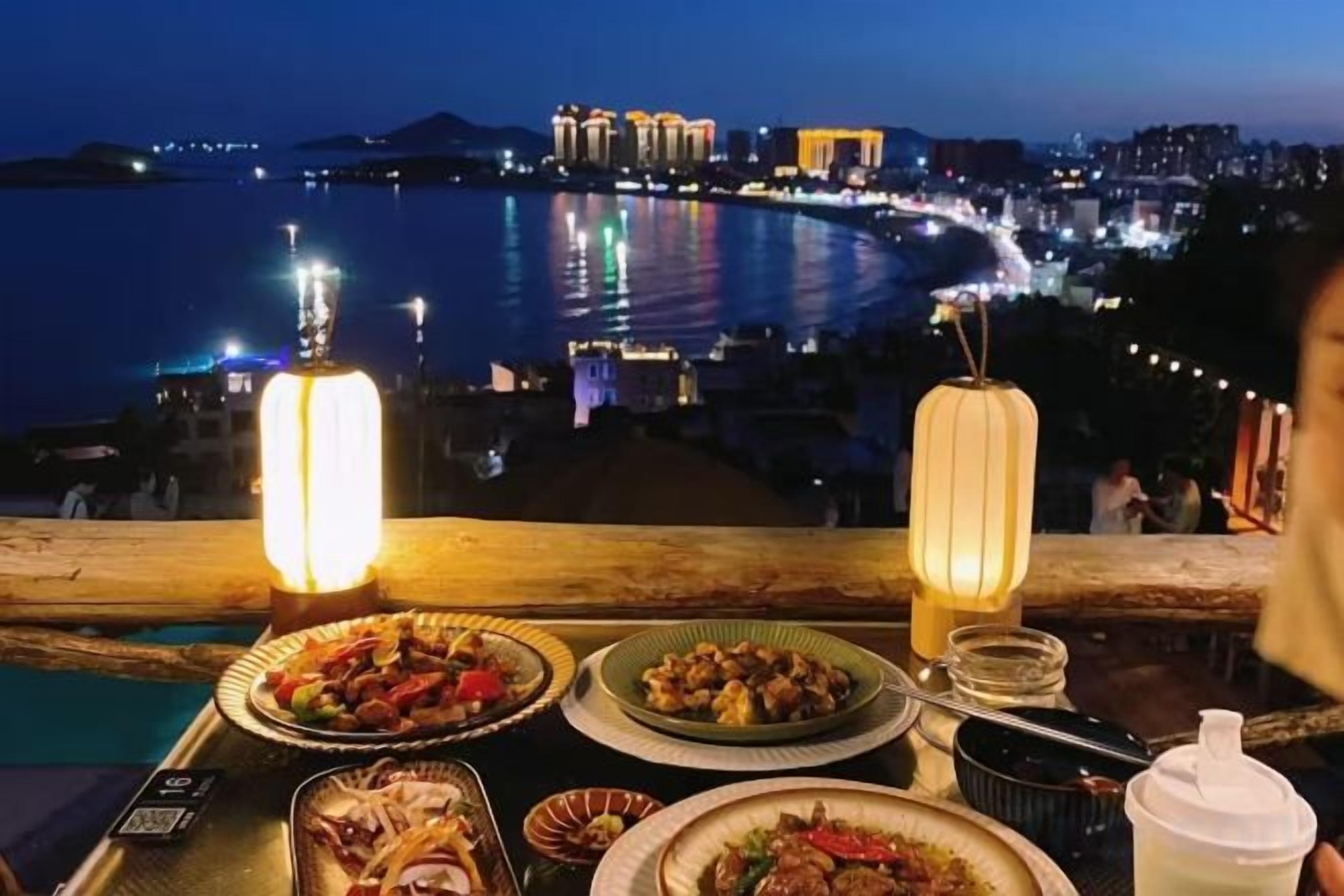A table with dishes and a view of a waterfront cityscape at night.