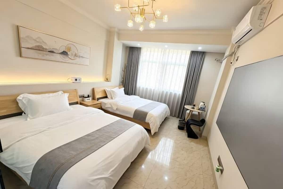 A hotel room with two beds, a desk, a chair, a TV, and a large window with curtains.