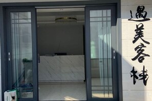 L’entrée d’un hôtel, avec une porte coulissante en verre, un comptoir d’accueil et une enseigne avec des caractères chinois.