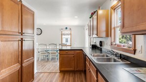 A kitchen with wooden cabinets, a double sink, and a dining area with chairs. - Best Kept Secret: Soundside, Hot Tub, Dogs OK (Kill Devil Hills)