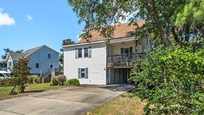 A two-story residential building with a front garage, a balcony on the second floor, and a driveway leading to a parked car. - Best Kept Secret: Soundside, Hot Tub, Dogs OK (Kill Devil Hills)