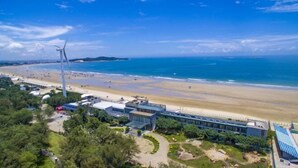 Un hotel frente al mar con vista a la playa, una turbina eólica y un edificio moderno con fachada de vidrio.
