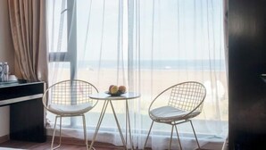 Una habitación con un ventanal grande, dos sillas, una mesita con fruta y un mueble oscuro.