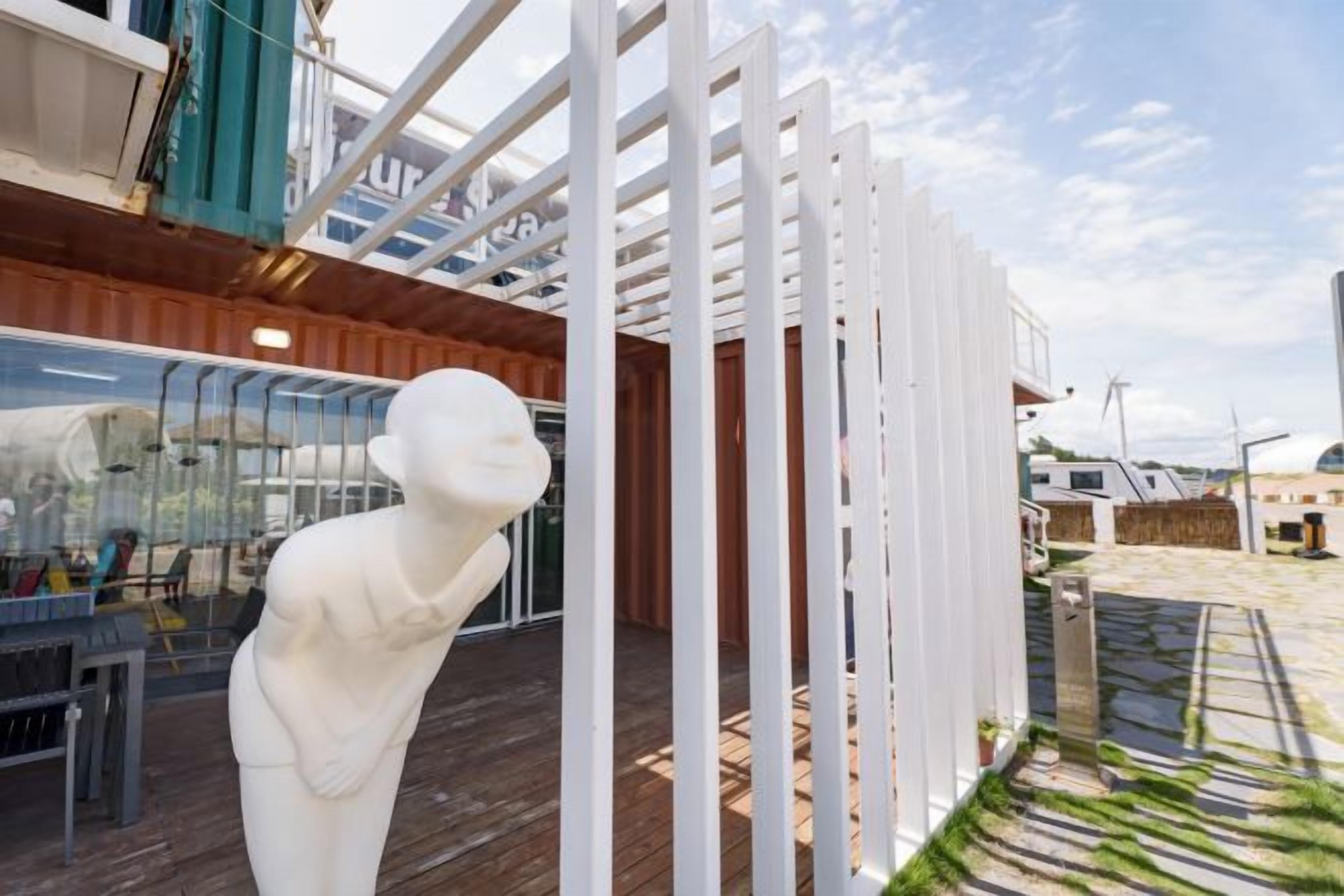 A white sculpture on a wooden deck with a glass enclosure and a white fence structure.