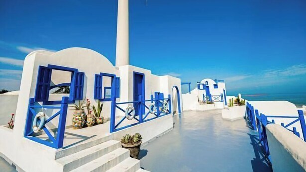 Un edificio blanco con detalles azules, una escalera y plantas en macetas.